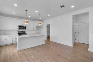 Kitchen featuring stainless steel appliances, white cabinets, a kitchen island with sink, and light wood-style floors