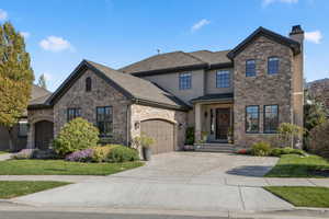 French country style house featuring a garage, concrete driveway, a chimney, and stone siding