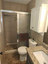 Full bath with vanity, a stall shower, and tile walls