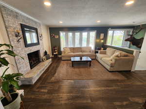 Living area with dark wood-style flooring, a brick fireplace, recessed lighting, healthy amount of natural light, and a textured ceiling