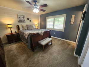 Bedroom featuring dark carpet, ceiling fan, a textured ceiling, and wood walls