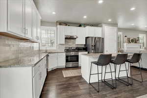 Kitchen with stainless steel appliances, white cabinets, a kitchen island, recessed lighting, and a kitchen bar