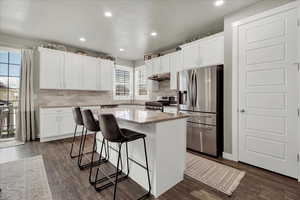 Kitchen with a breakfast bar, stainless steel appliances, white cabinetry, decorative backsplash, and recessed lighting