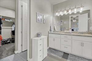 Bathroom featuring double vanity, ensuite bathroom, a spacious closet, a ceiling fan, and light tile patterned floors