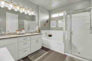 Bathroom with double vanity, a stall shower, a garden tub, and dark tile patterned flooring