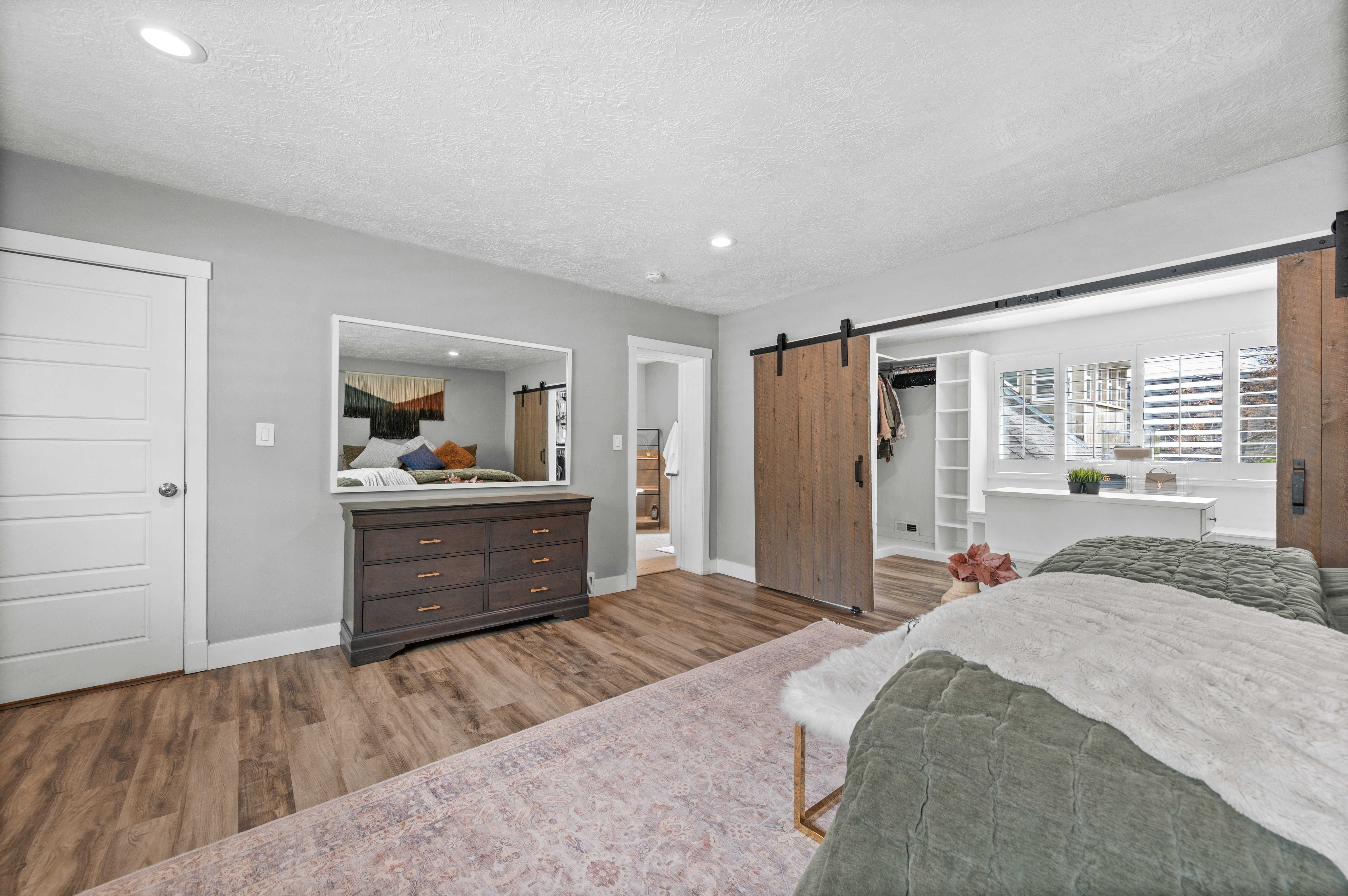 Bedroom featuring a barn door, wood finished floors, a spacious closet, recessed lighting, and a textured ceiling