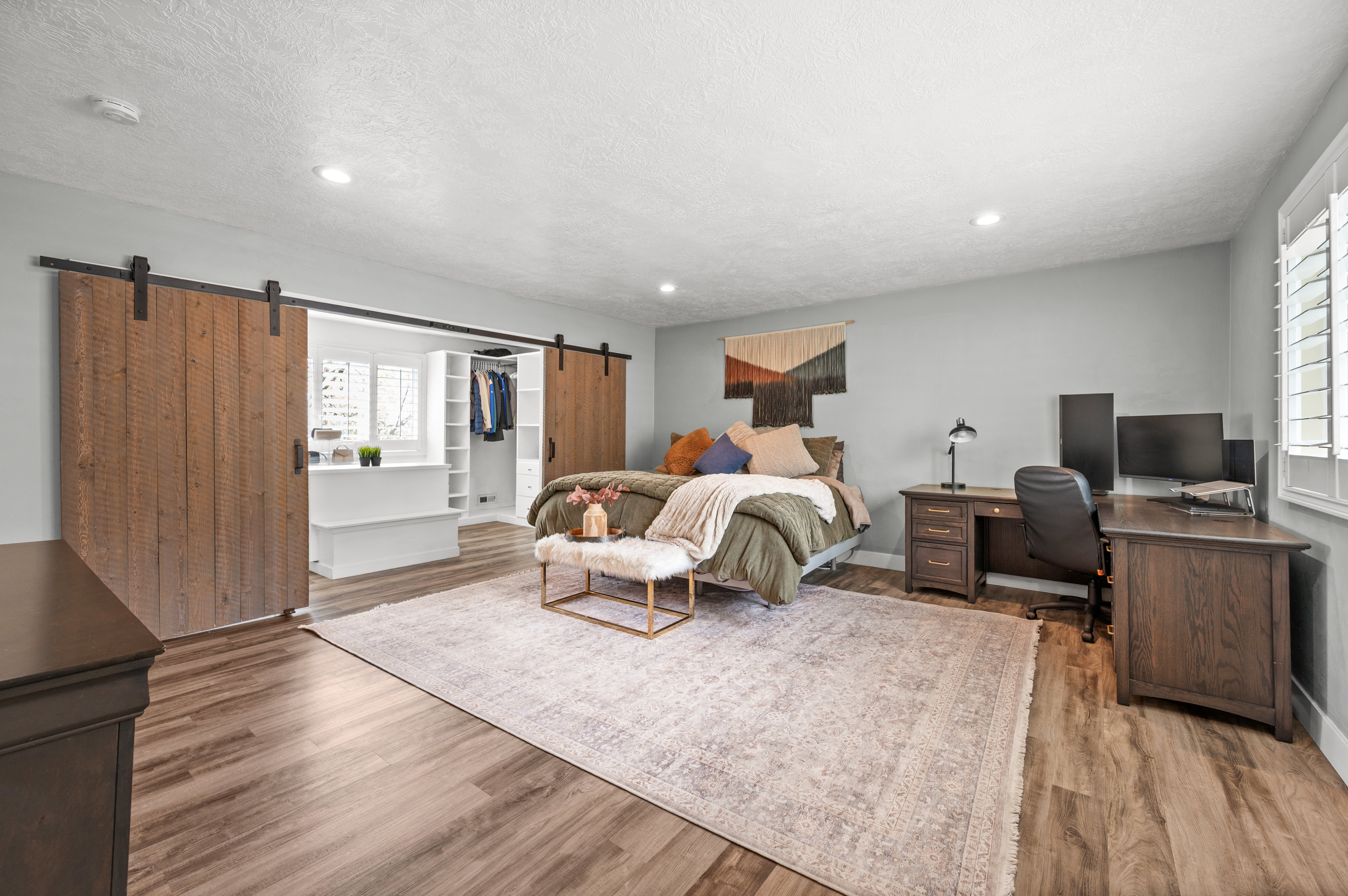 Bedroom featuring a barn door, a spacious closet, a desk, light wood-style floors, and recessed lighting