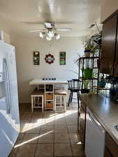 Kitchen featuring a textured ceiling, white appliances, light tile patterned floors, dark wood finish cabinets, and a ceiling fan