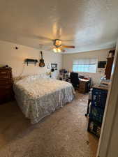 Carpeted bedroom with a textured ceiling, an office area, and ceiling fan