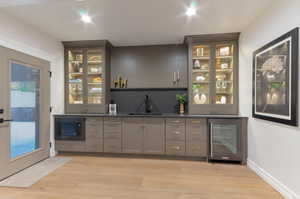 Indoor wet bar with glass fronted cabinets, gray cabinetry, beverage cooler, and built in microwave