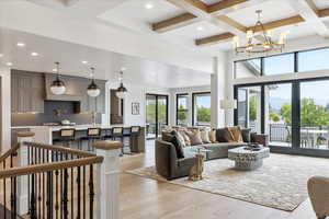 Living room with light wood finished floors, coffered ceiling, french doors, and hanging lights