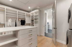 Walk in closet with stacked washer and clothes dryer and light wood finished floors