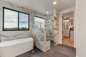 Full bath with a marble finish shower, a freestanding tub, a walk in closet, dark tile patterned floors, and recessed lighting
