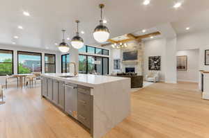 Kitchen featuring open floor plan, a center island with sink, light wood-style flooring, and a stone fireplace