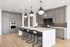 Kitchen featuring gray cabinetry, light stone countertops, a breakfast bar area, decorative backsplash, and light wood-type flooring