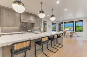 Kitchen with light stone counters, a kitchen bar, light wood finished floors, gray cabinetry, and backsplash