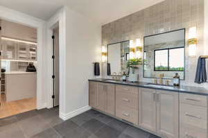 Bathroom featuring double vanity, tasteful backsplash, a walk in closet, dark tile patterned floors, and a shower with shower door
