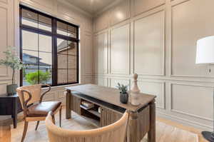 Office space with a decorative wall, ornamental molding, and light wood-style flooring