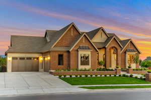 View of front of house with a front yard, brick siding, roof with shingles, a garage, and driveway