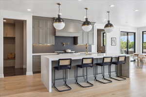 Kitchen with light stone counters, a large island, light wood finished floors, a breakfast bar, and pendant lighting