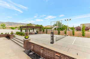 Fenced backyard featuring a pergola, a mountain view, a patio, basketball hoop, and an outdoor living space