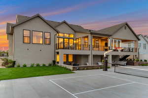 Back of house at dusk with stucco siding, a patio area, a balcony, and roof with shingles