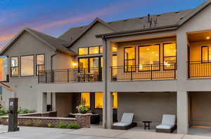 Back of house at dusk featuring stucco siding, roof with shingles, and a patio
