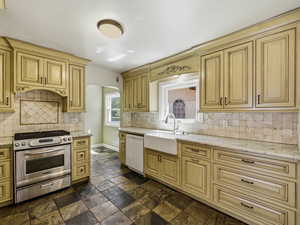 Kitchen with stainless steel gas stove, white dishwasher, light stone counters, stone tile floors, and arched walkways