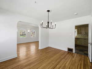 Unfurnished dining area with ornamental molding, dark wood finished floors, arched walkways, and suspended lighting