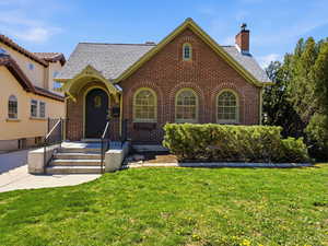 View of front of house featuring brick siding, a front yard, a chimney, and roof with shingles