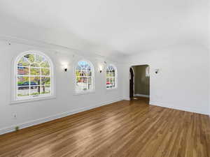 Spare room with arched walkways, dark wood-style floors, healthy amount of natural light, and ornamental molding