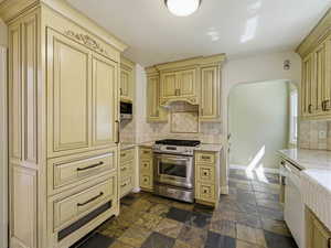 Kitchen with arched walkways, stainless steel appliances, cream cabinets, backsplash, and light stone countertops