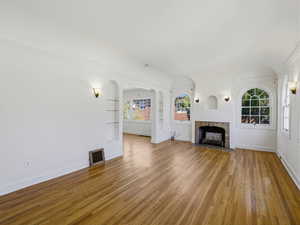 Unfurnished living room featuring a fireplace with flush hearth, hardwood / wood-style floors, crown molding, and arched walkways