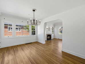 Unfurnished living room featuring hanging lights, dark wood-style flooring, ornamental molding, a brick fireplace, and arched walkways