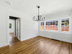 Unfurnished dining area featuring dark wood-type flooring, crown molding, and hanging lights