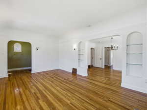 Unfurnished living room featuring arched walkways, built in shelves, dark wood-style flooring, a chandelier, and crown molding