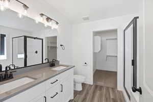 Full bath with a spacious closet, a stall shower, double vanity, and dark wood finished floors