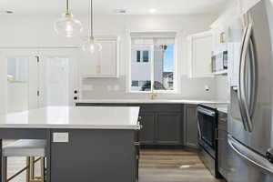 Two tone kitchen with two tone cabinets, stainless steel appliances, a breakfast bar area, dark wood-style flooring, and decorative light fixtures