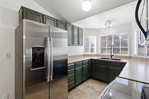 Kitchen with green cabinets, stainless steel refrigerator with ice dispenser, electric range, and lofted ceiling