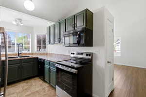 Kitchen with black appliances, green cabinets, plenty of natural light, and light countertops