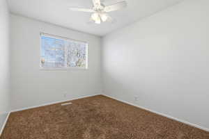 Empty room featuring dark colored carpet and a ceiling fan