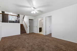 Unfurnished living room featuring dark carpet and a ceiling fan