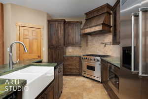 Kitchen with dark wood finish cabinetry, high end appliances, dark stone countertops, and light stone finish flooring