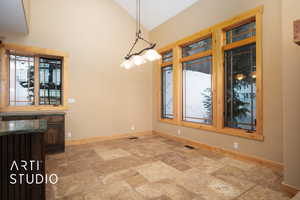 Unfurnished dining area featuring stone tile flooring and vaulted ceiling