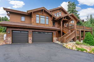 View of front facade featuring a garage, stone siding, driveway, a deck, and roof with shingles