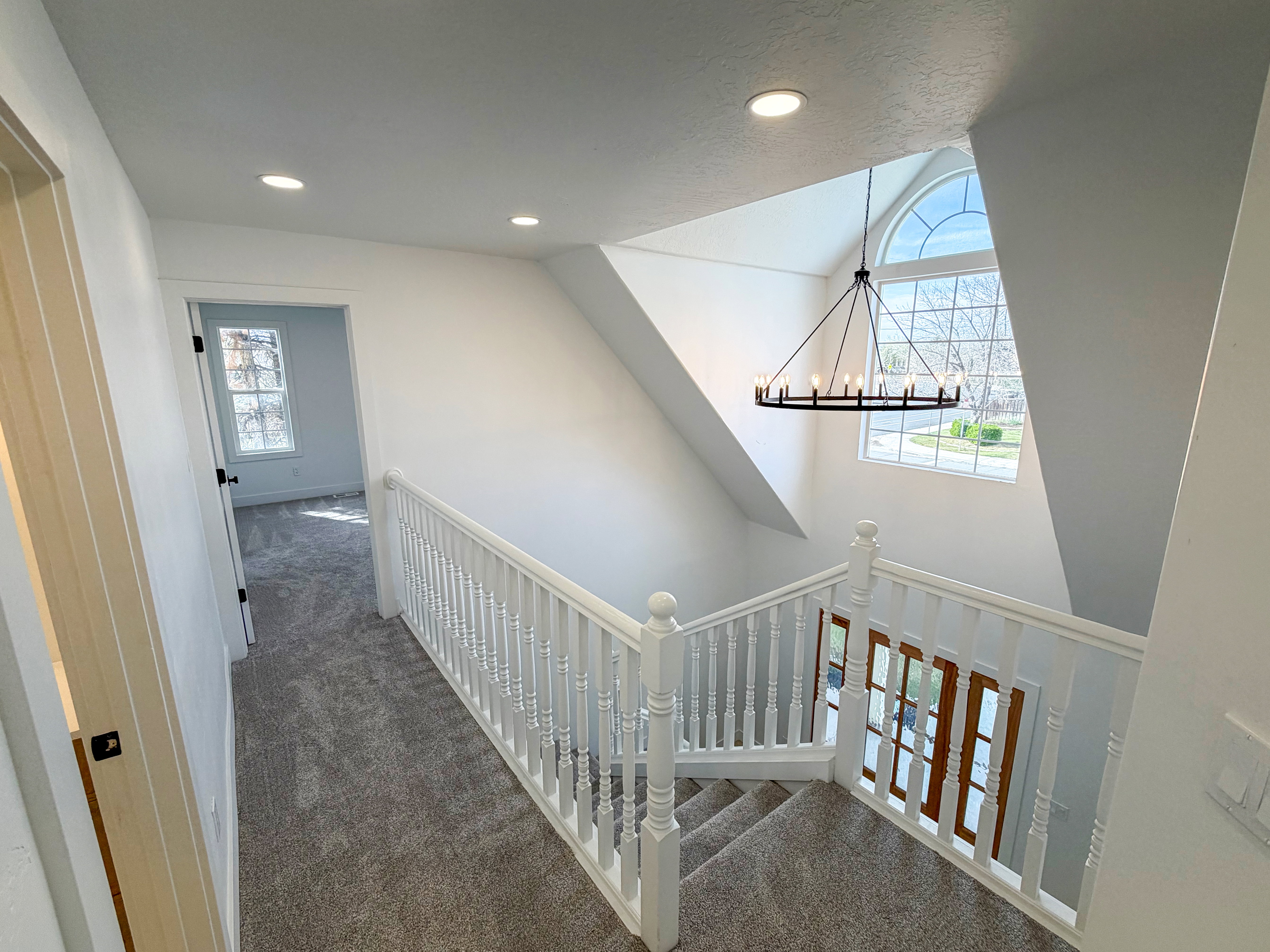 Hallway with dark carpet, a chandelier, and an upstairs landing