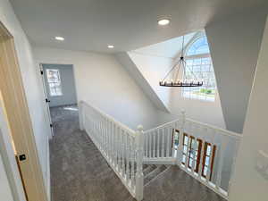 Hallway with dark carpet, a chandelier, and an upstairs landing