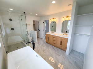 Full bathroom featuring double vanity, a freestanding tub, a stall shower, recessed lighting, and light marble finish floors