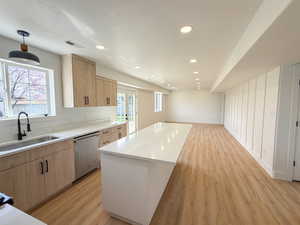 Kitchen with light wood finish cabinets, dishwasher, light wood finished floors, light stone counters, and open floor plan