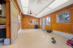 Miscellaneous room with wooden walls, vaulted ceiling, concrete flooring, and ceiling fan